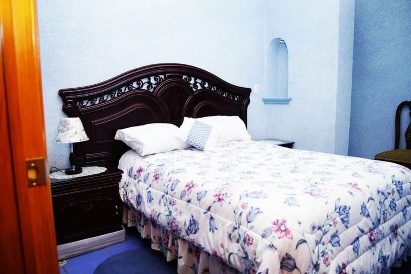 Cama matrimonial con edredón floral en tonos azules en la habitación sencilla del Hotel Ejecutivo Inn